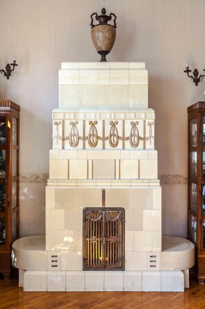 A fireplace with a decorative urn on top, surrounded by white tiles with gold accents. - Pałac Brzezno (Prusice)