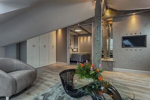 Uma sala de estar moderna com um sofá, uma mesa de centro de vidro com flores e uma TV fixada numa parede texturizada.