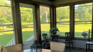 Een eetruimte met een ronde houten tafel, zes stoelen en uitzicht op een golfbaan door grote ramen.