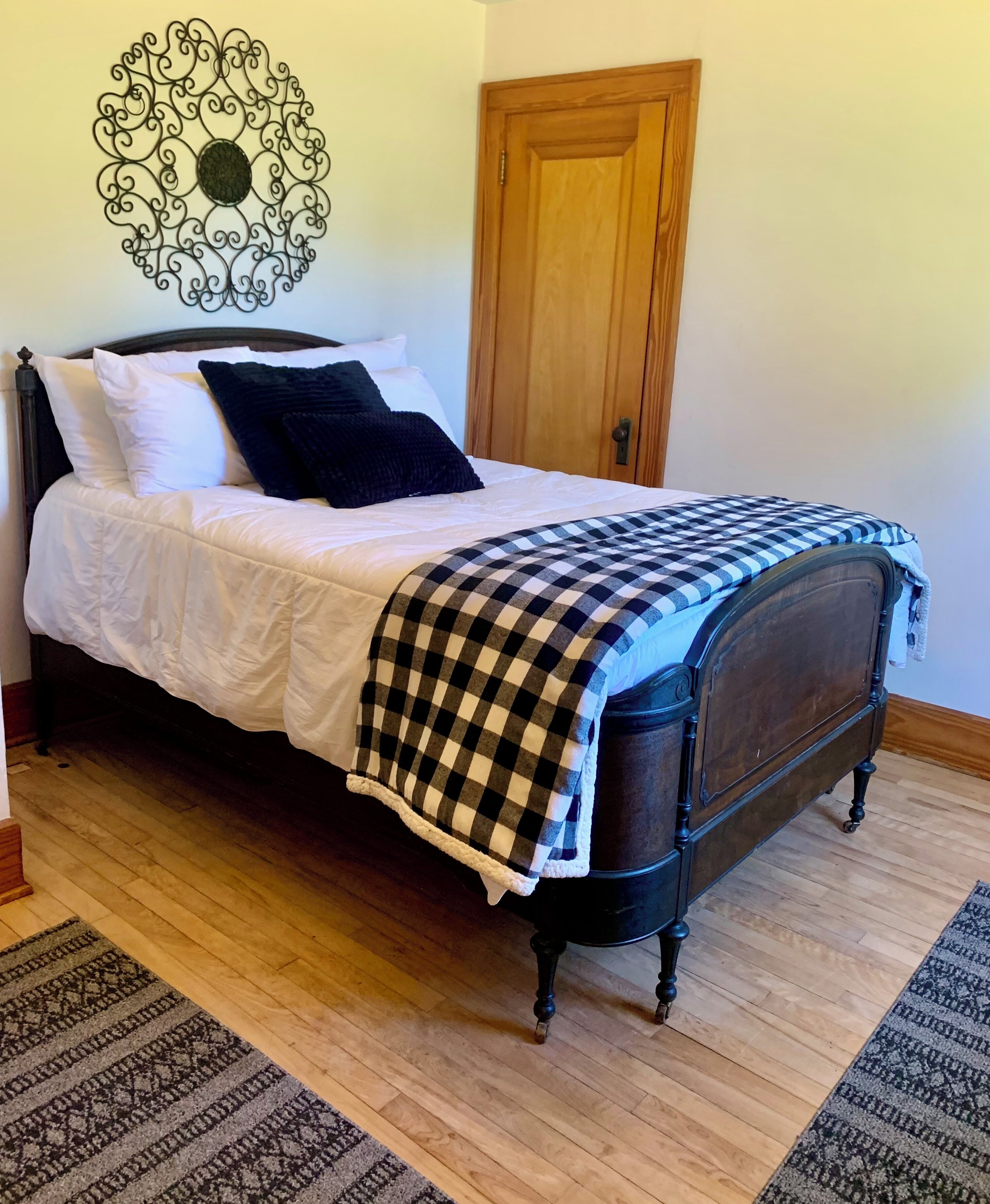A bed with a checkered blanket, a dark headboard, and a decorative wall piece.