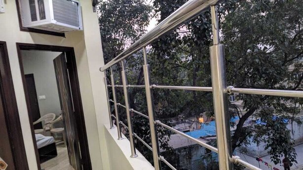 A balcony with metal railings overlooking a residential area with trees and a blue tarp-covered structure.