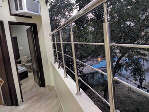 A balcony with metal railings overlooking a residential area with trees and a blue tarp-covered structure. - Mye home Stay is located near golden temple , (INA Colony)