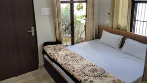 A bedroom with a bed, a window with curtains, a door, and a potted plant outside.