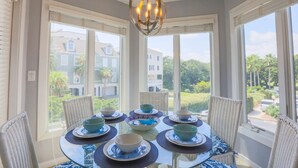 En matplats med ett glasbord för sex personer, omgiven av flätade stolar, stora fönster med persienner och en hängande lampa.