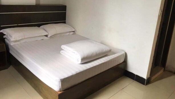 A neatly made bed with white linens and pillows in a room with a dark headboard and plain walls. - ruixing hotel (Yangjiang)