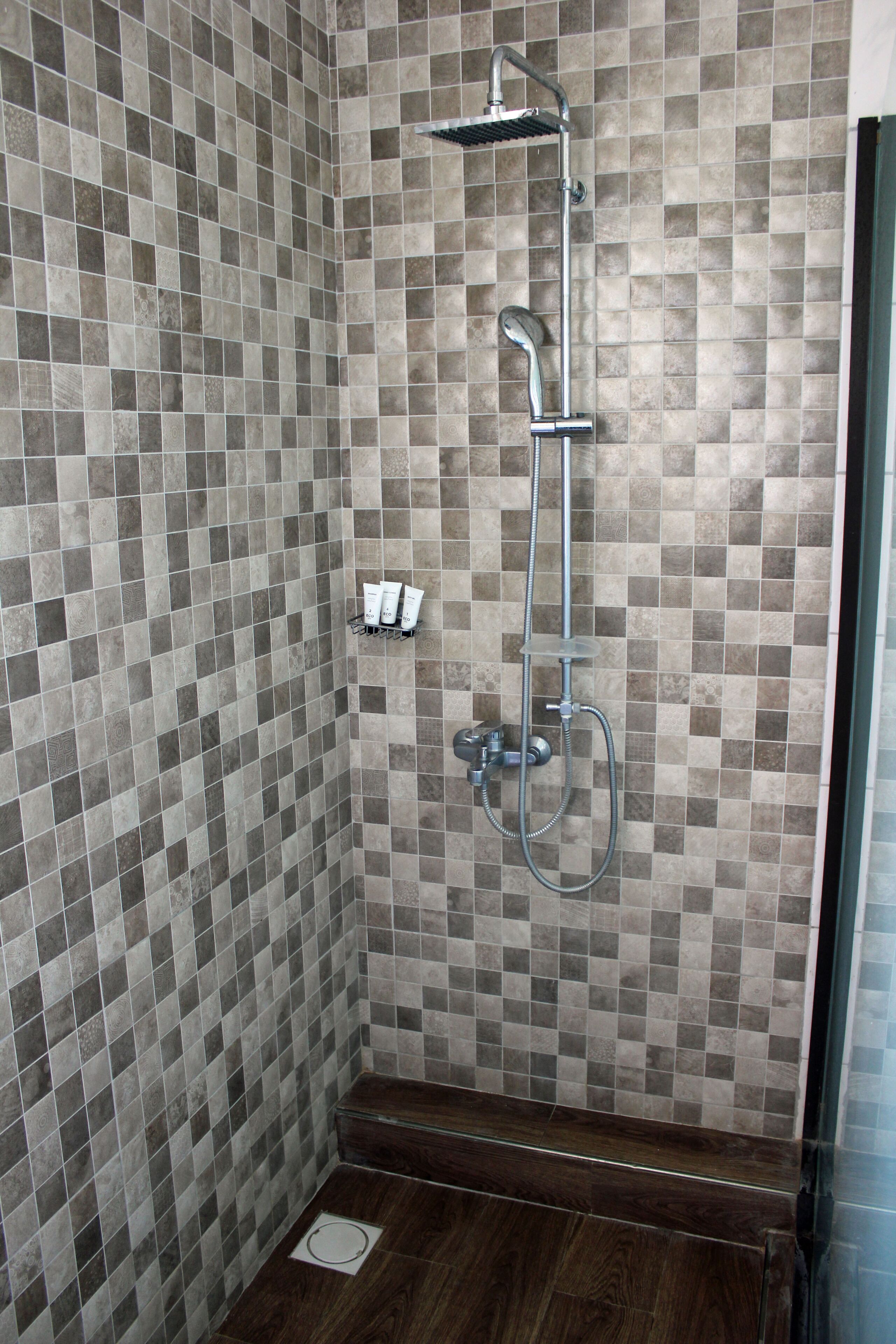 A shower area with a tiled wall, a handheld showerhead, and a wall-mounted faucet.