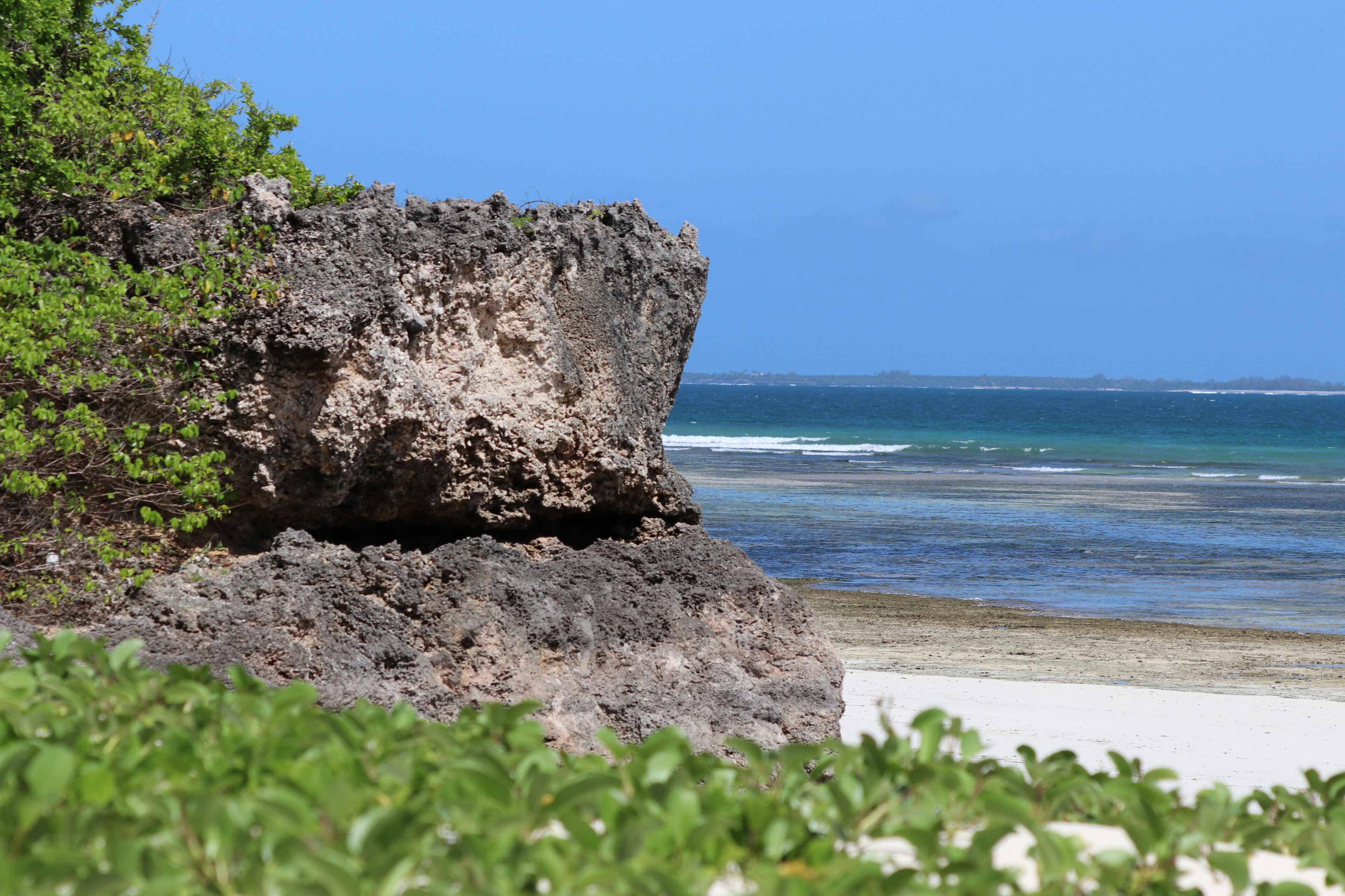 A rocky cliff with a beach in the foreground and ocean in the background.