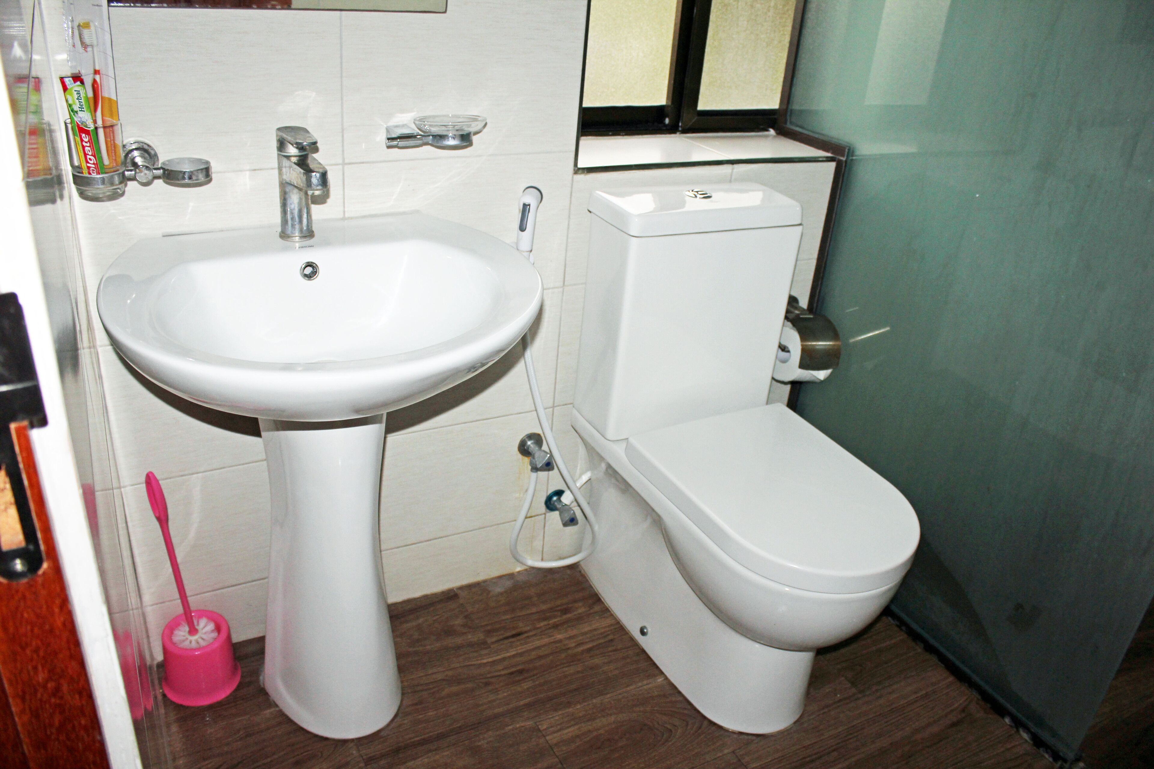 A bathroom with a white sink, toilet, and a pink toilet brush.