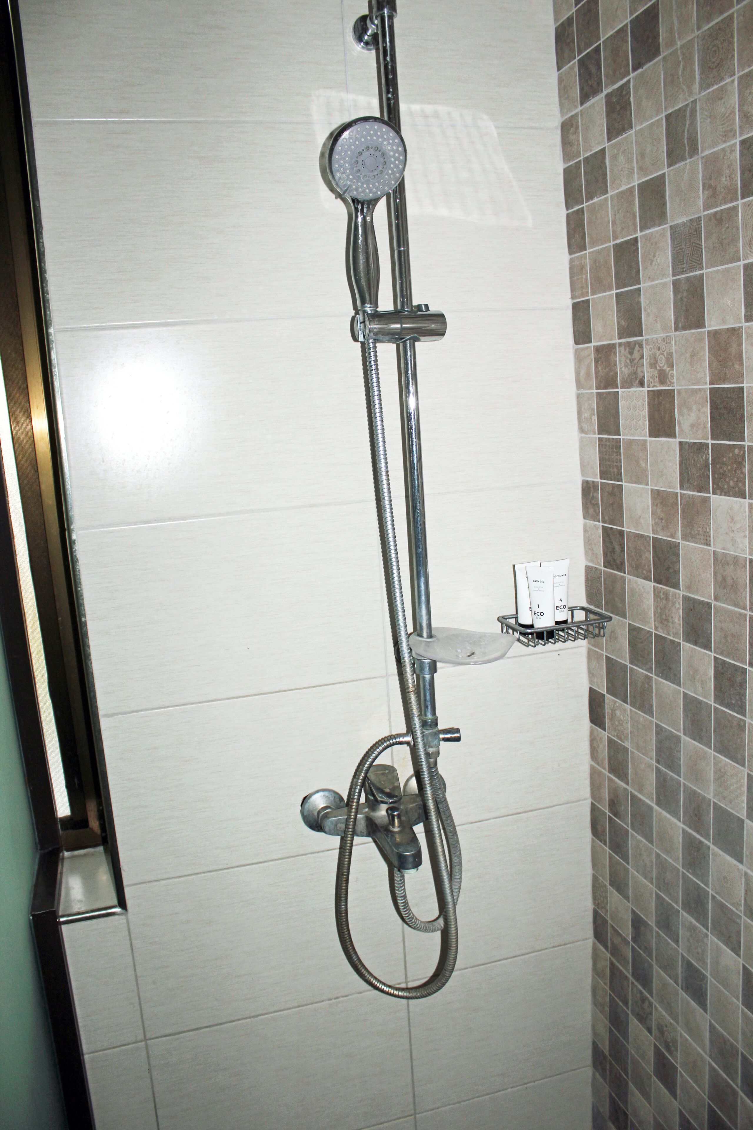 A shower with a handheld showerhead and a wall-mounted control.