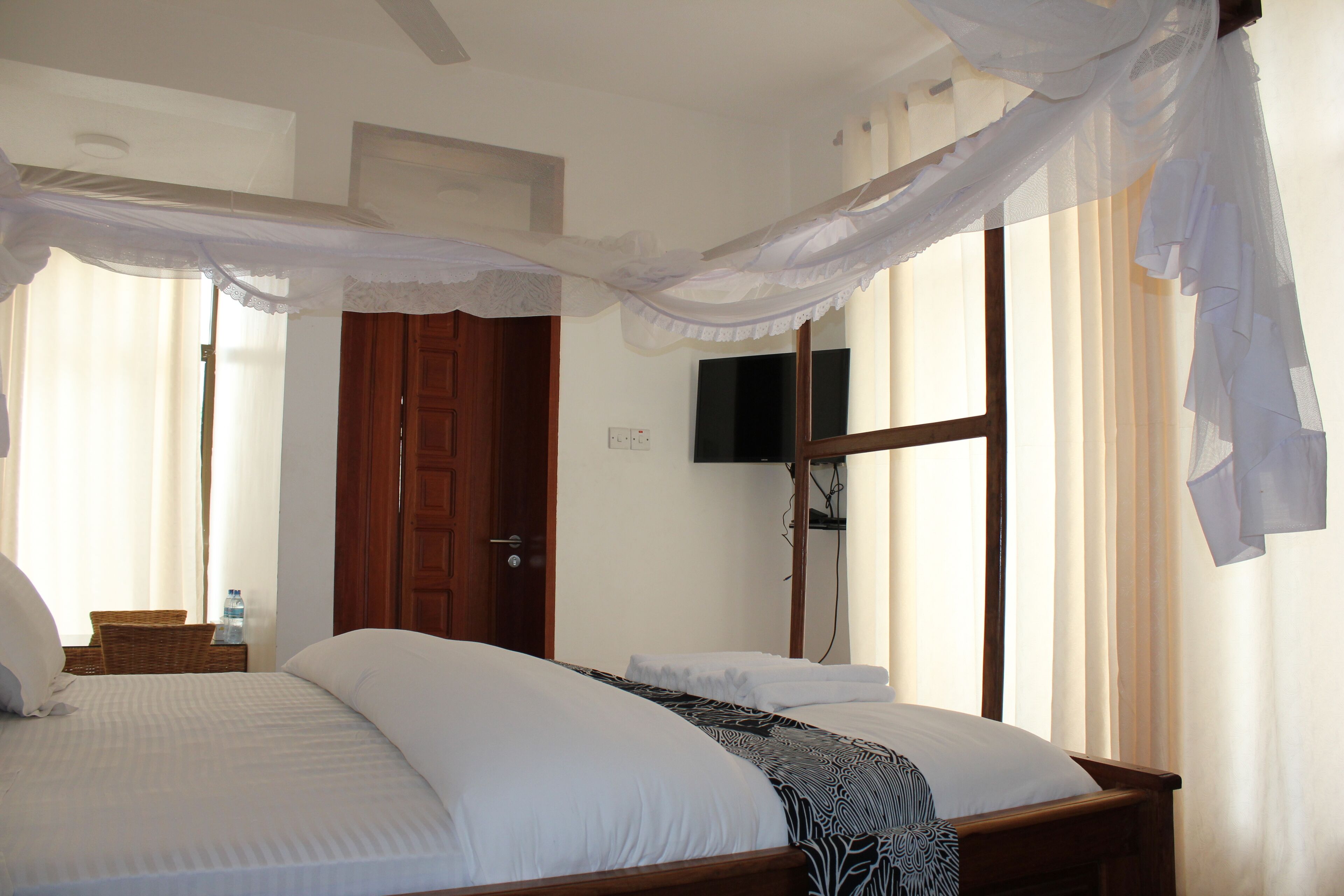 A bedroom with a bed, a wooden door, a television on the wall, and a window with curtains.