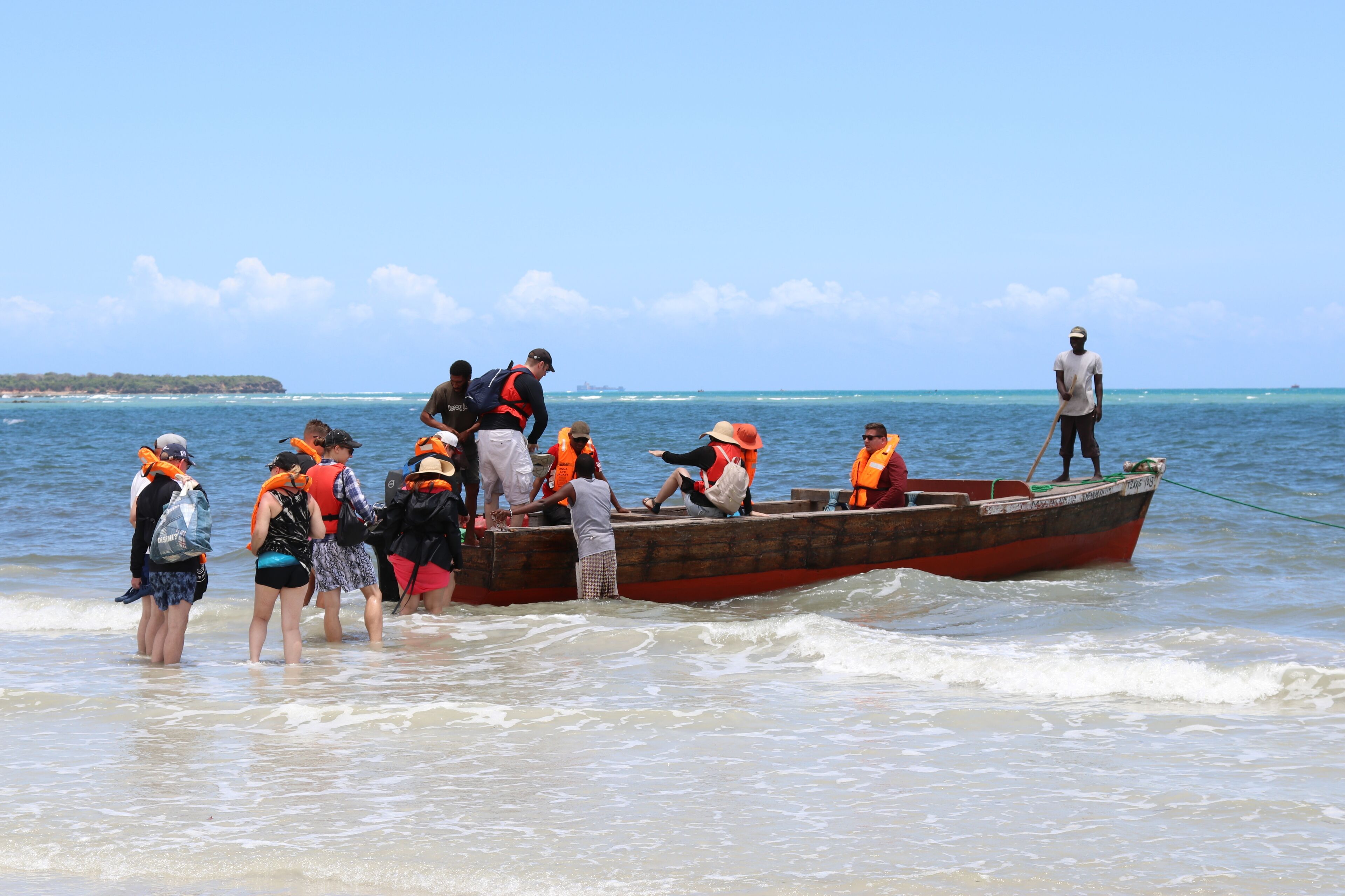 A group of people on a boat at the beach, some wearing life jackets.