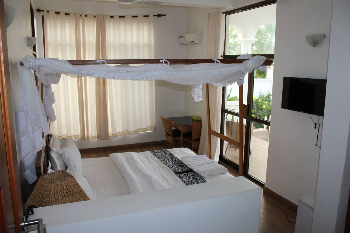 Una camera d'albergo con un letto, una televisione, una finestra con tende, una sedia e un tavolo.