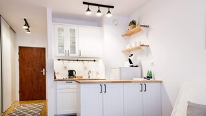 A compact kitchen with white cabinets, a wooden countertop, and a built-in oven. There are hanging lights above the sink and a small plant on a shelf. - Arkadia Chillout Apartment (Warsaw)