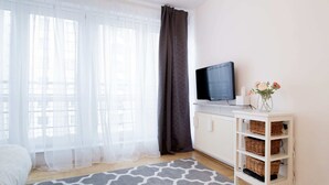 A hotel room with a bed, a television on a white cabinet, a grey patterned rug, and a white shelf with baskets. - Arkadia Chillout Apartment (Warsaw)
