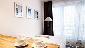 A hotel room with a bed, a table with two cups, a lamp, and three framed pictures on the wall. - Arkadia Chillout Apartment (Warsaw)