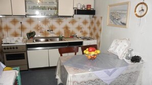 Een kleine keuken met essentiële apparaten, een eettafel met een schaal fruit en een kleine koelkast.