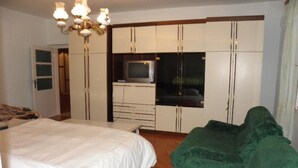 Een slaapkamer met een bed, een groene bank, een televisie op een kast en een kroonluchter.