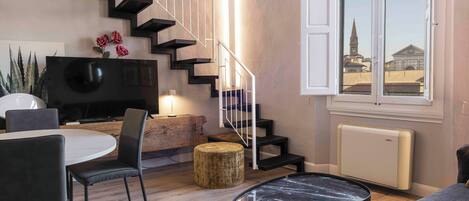 Un salon moderne avec un escalier, un coin repas et une vue sur un immeuble par la fenêtre.