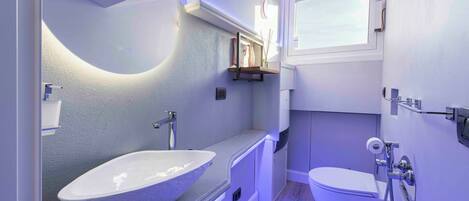 A modern bathroom with a large vessel sink, a toilet, and a shower.