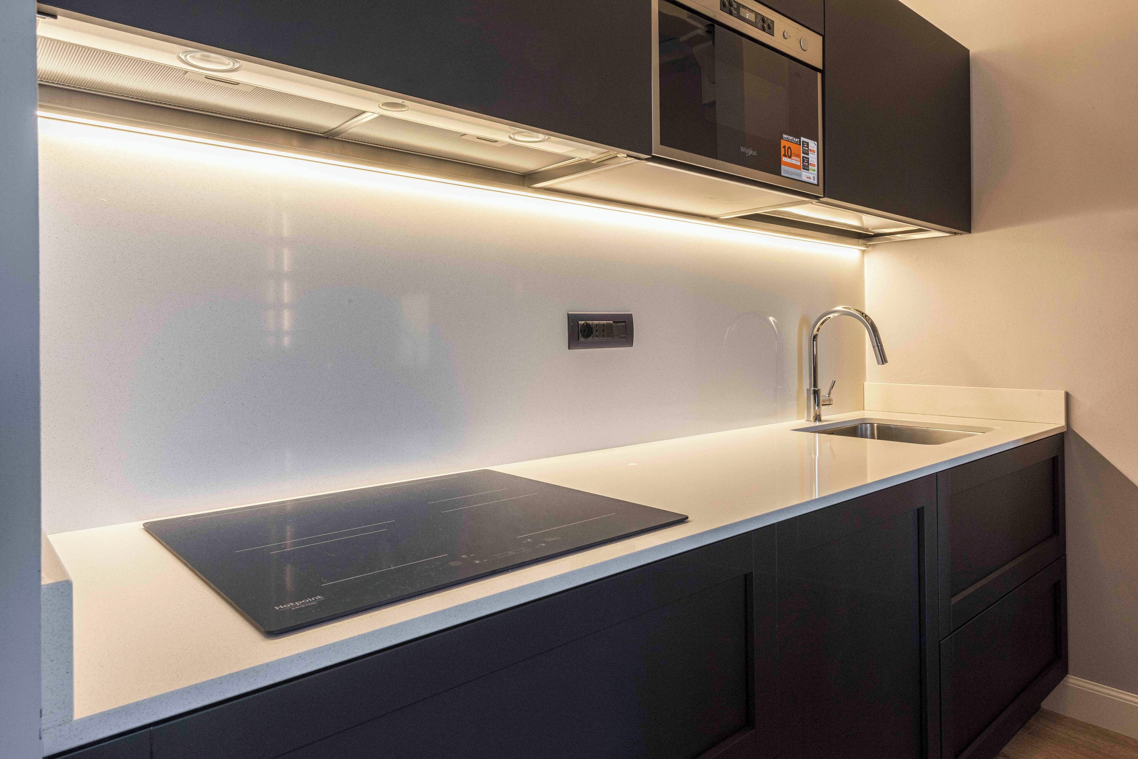Une cuisine moderne dotée d’une plaque de cuisson à induction intégrée, d’un évier en acier inoxydable et de meubles de rangement aux couleurs sombres.