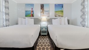 A hotel room with two beds, a nightstand with a lamp, and three wall-mounted paintings depicting coastal scenes. - The Inn at Southport (Southport)