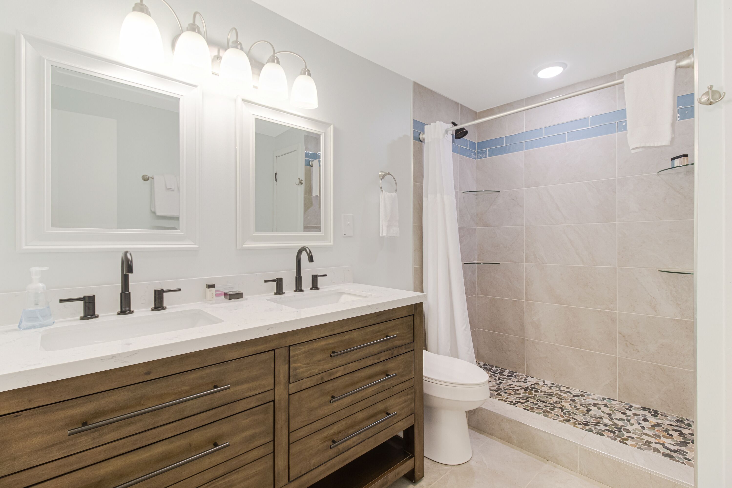 A bathroom with a double sink vanity, a toilet, and a shower area.