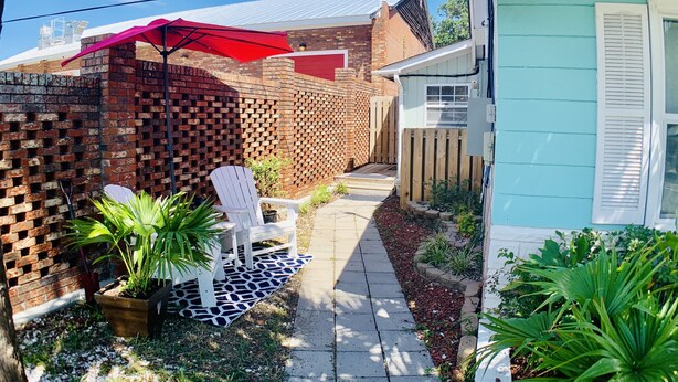 A backyard with a brick wall, a wooden fence, a red umbrella, a white chair, and a small shed. - The Inn at Southport (Southport)