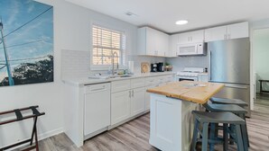 A modern kitchen with white cabinets, a wooden island, and bar stools. - The Inn at Southport (Southport)