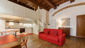 Un salón amplio con un sofá rojo, suelo de madera y una cocina al fondo.