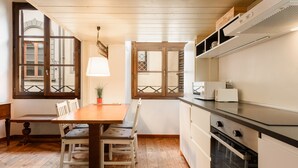 Una cocina con piso de madera, una mesa de comedor con sillas, horno empotrado y ventana con vista a la calle.
