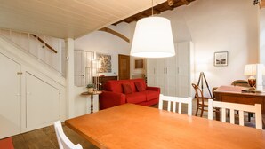 Un comedor con mesa y sillas de madera, un sofá rojo y una escalera con paredes blancas y vigas de madera.
