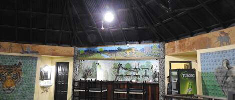 A restaurant with a high ceiling, wooden chairs, a dining table, and a mural depicting a savannah scene.