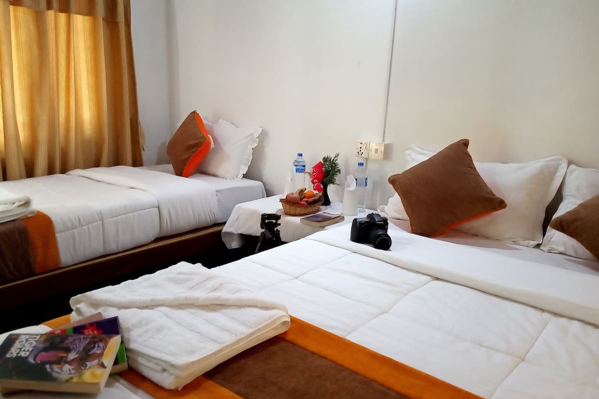 Une chambre d’hôtel avec deux lits simples, une petite table sur laquelle se trouve un panier de fruits, un appareil photo et un livre, le tout placé du côté gauche.