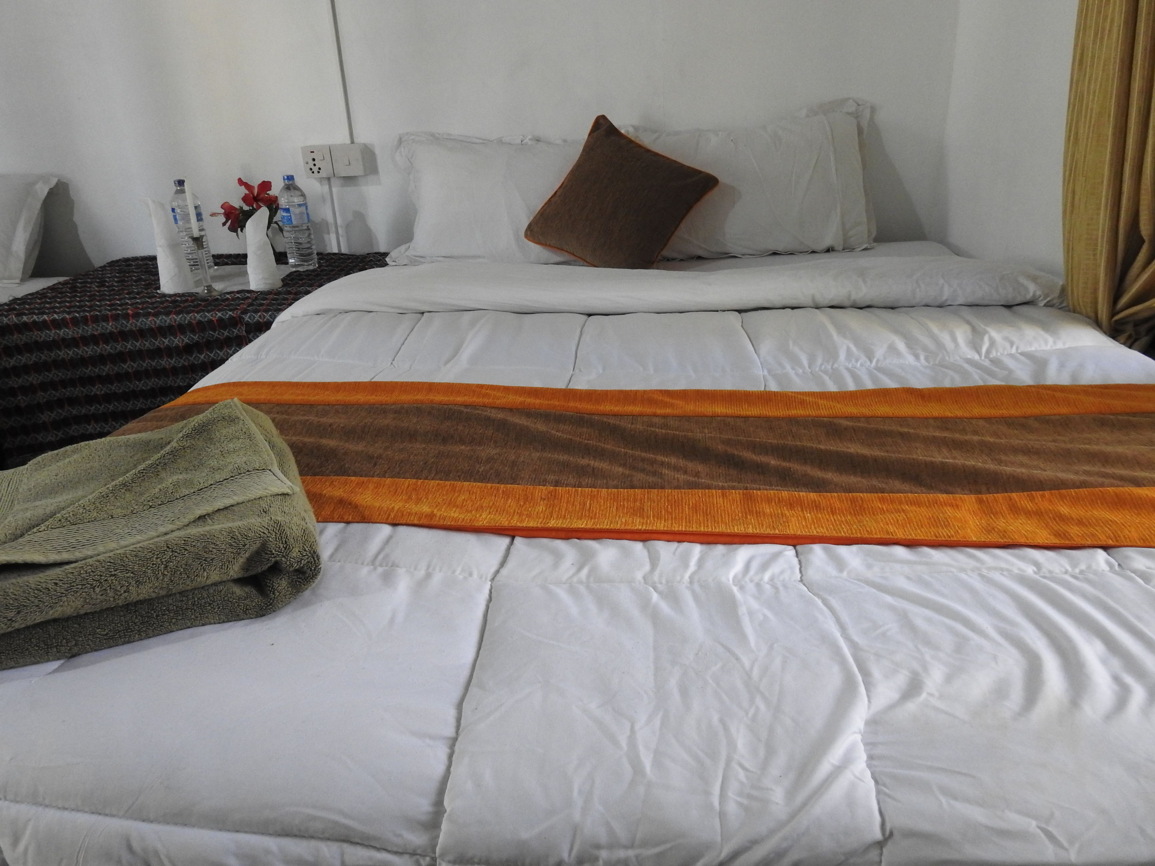 Une chambre d’hôtel avec un lit, des oreillers, une couverture et une table de chevet sur laquelle se trouvent des bouteilles et une lampe.
