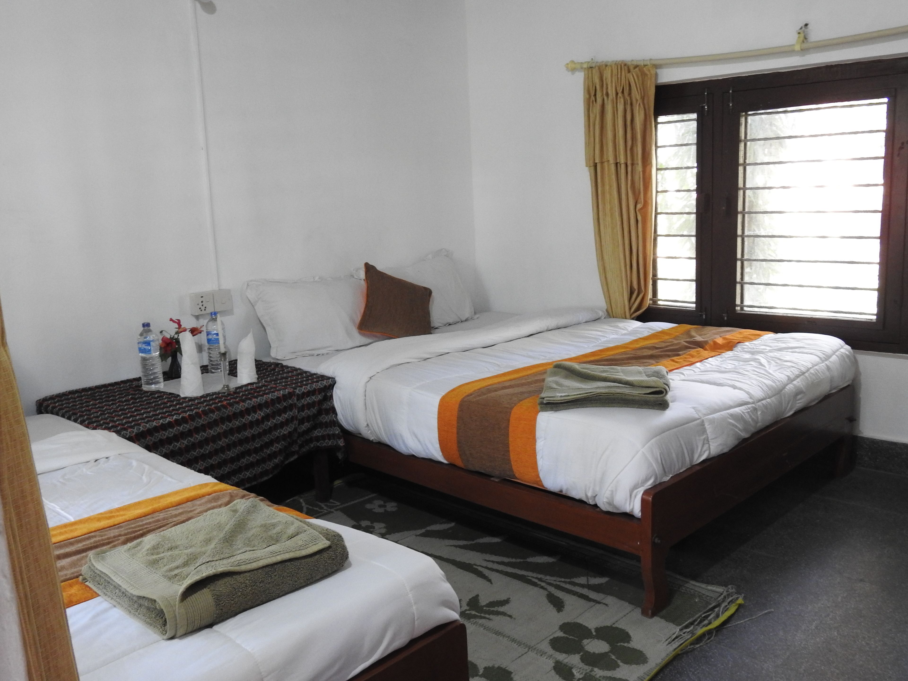 Una habitación de hotel con dos camas, una mesita de noche, un ventanal con cortinas y un tapete estampado con motivos florales.