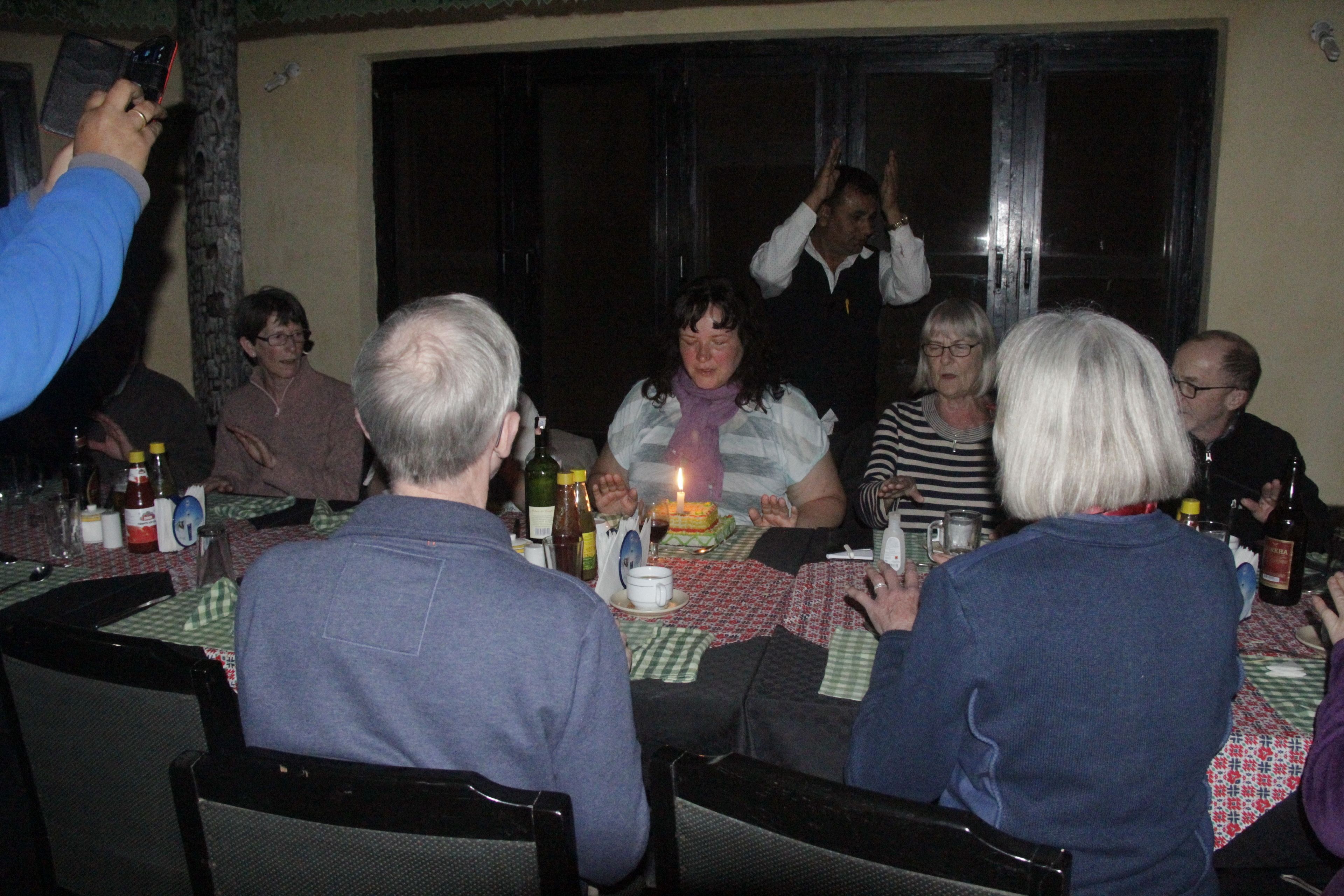 A group of people seated around a table with a candle on it, suggesting a celebration or gathering.