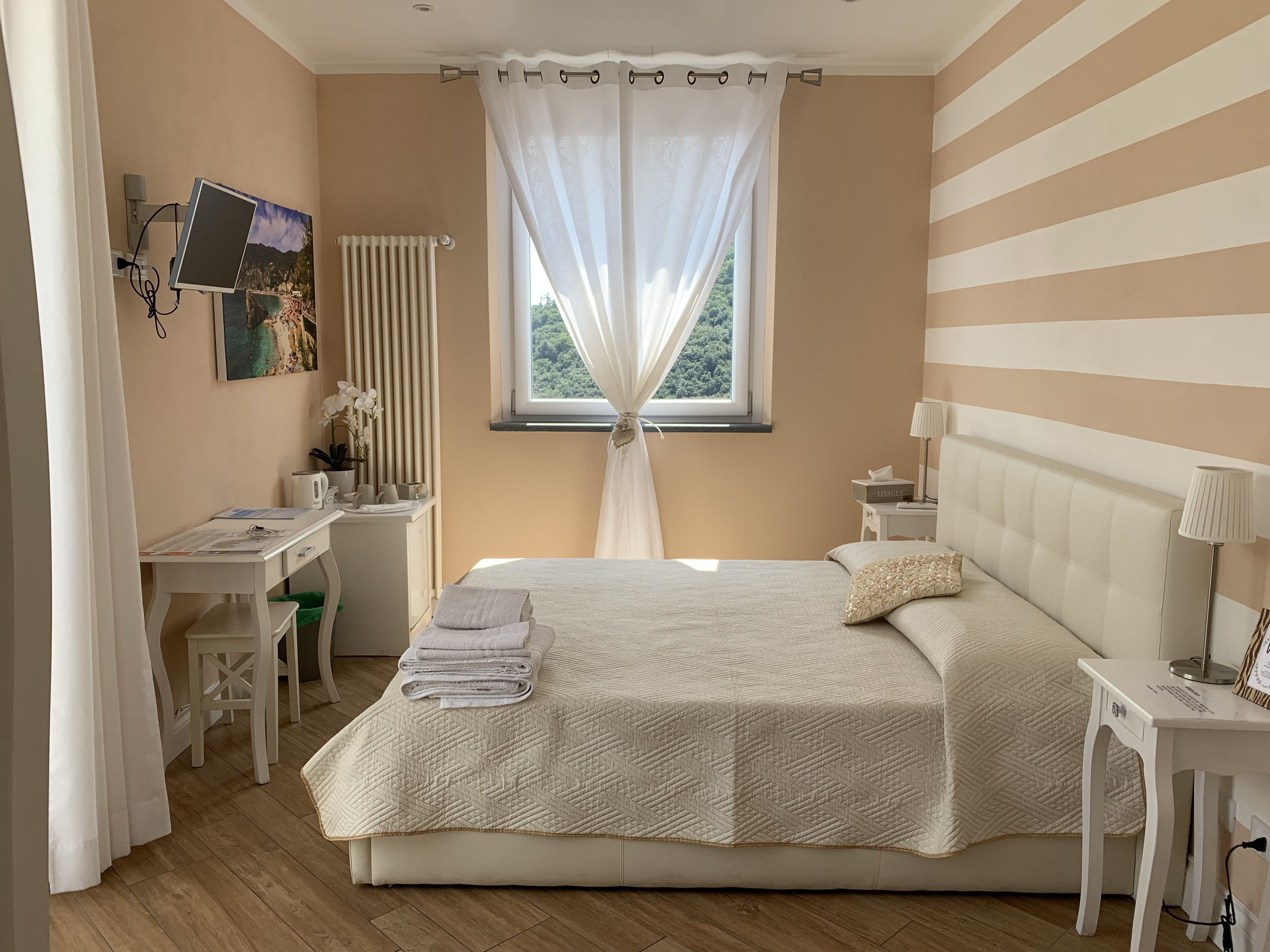 A bedroom with a bed, bedside tables, a desk, a radiator, and a window with curtains.