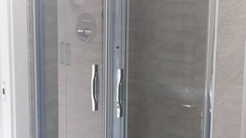 Une douche fermée par des parois de verre, dotée d’un panneau de commande, d’un pommeau de douche à main et d’un sol carrelé.