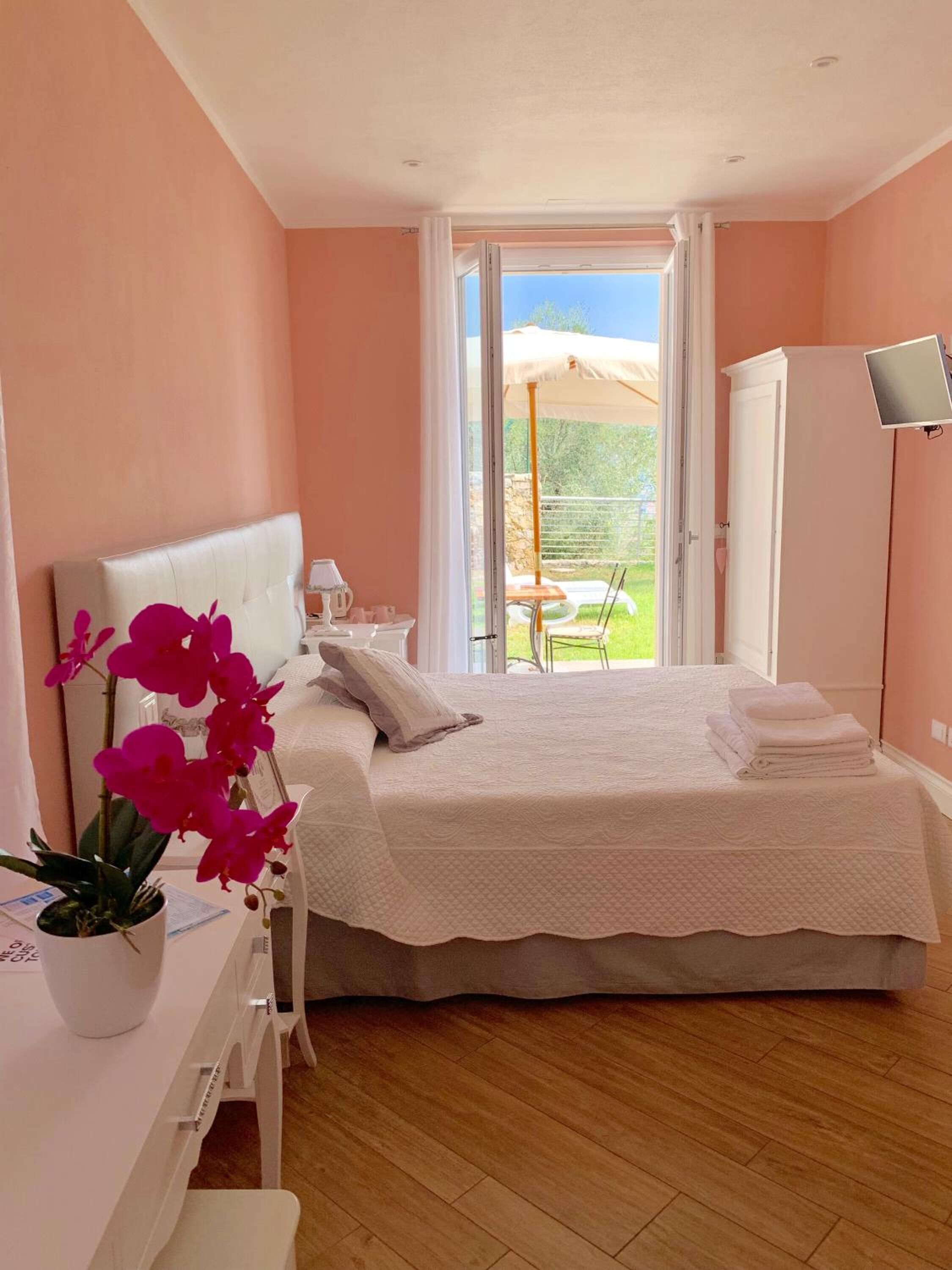 A bedroom with a bed, a desk, a potted orchid, and a view of the outdoors through a sliding door.