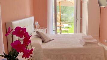 A bedroom with a bed, a desk, a potted orchid, and a view of the outdoors through a sliding door.