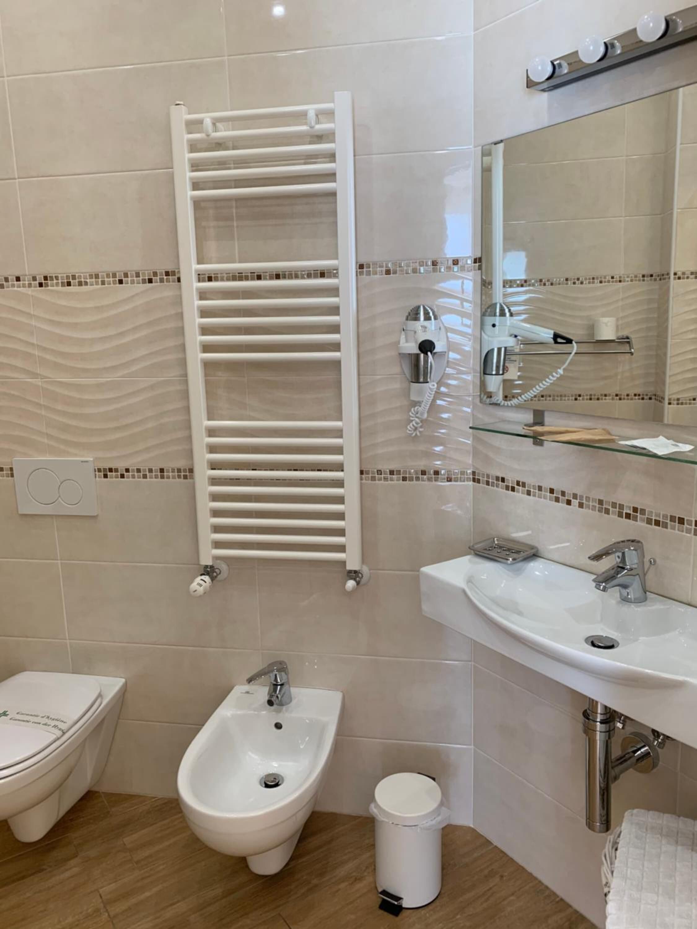 Ein Badezimmer mit einer Bidet, einem Waschbecken, einem Spiegel, einem Handtuchhalter und einem Föhn.