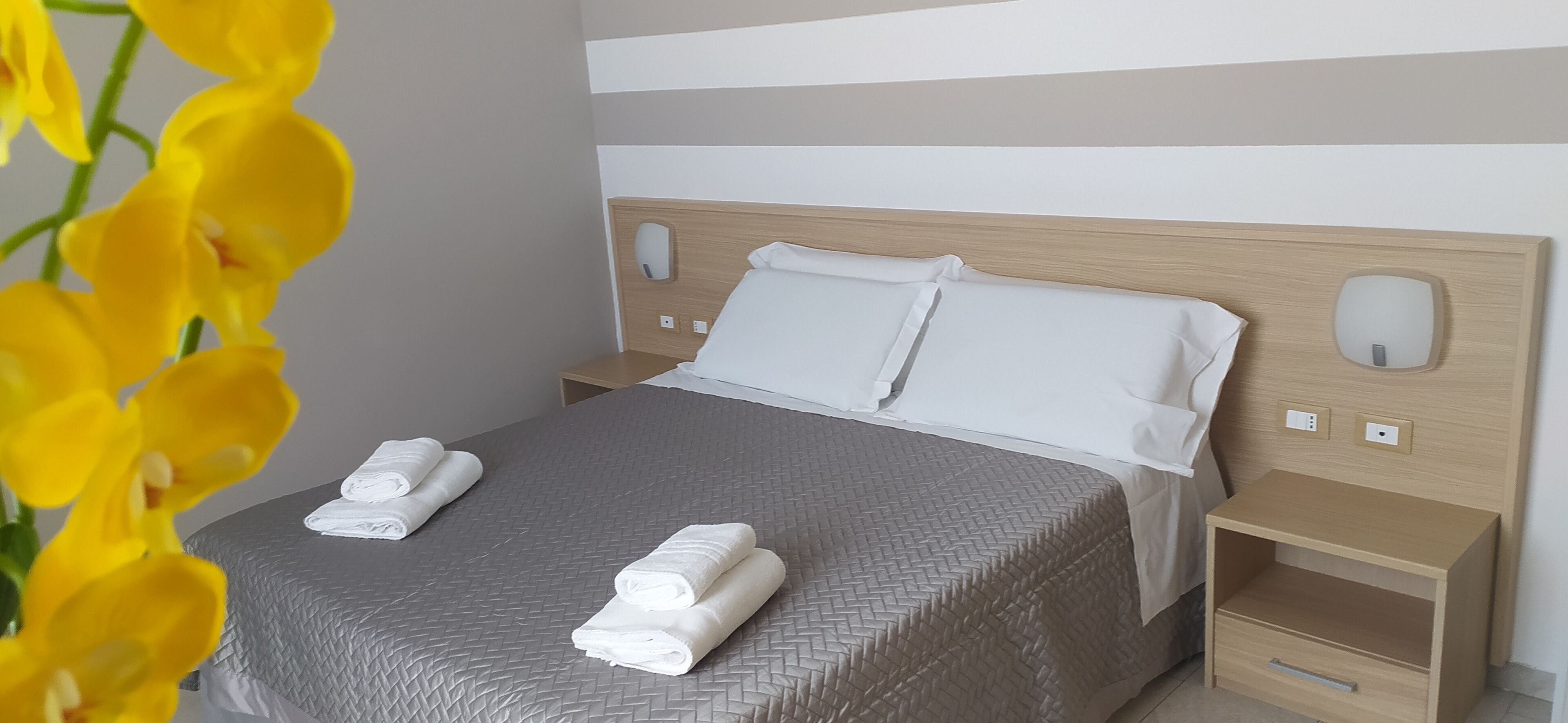 Un lit bien fait, avec du linge de lit blanc, une couvre-lit grise à texture et deux tables de chevet avec des lampes.
