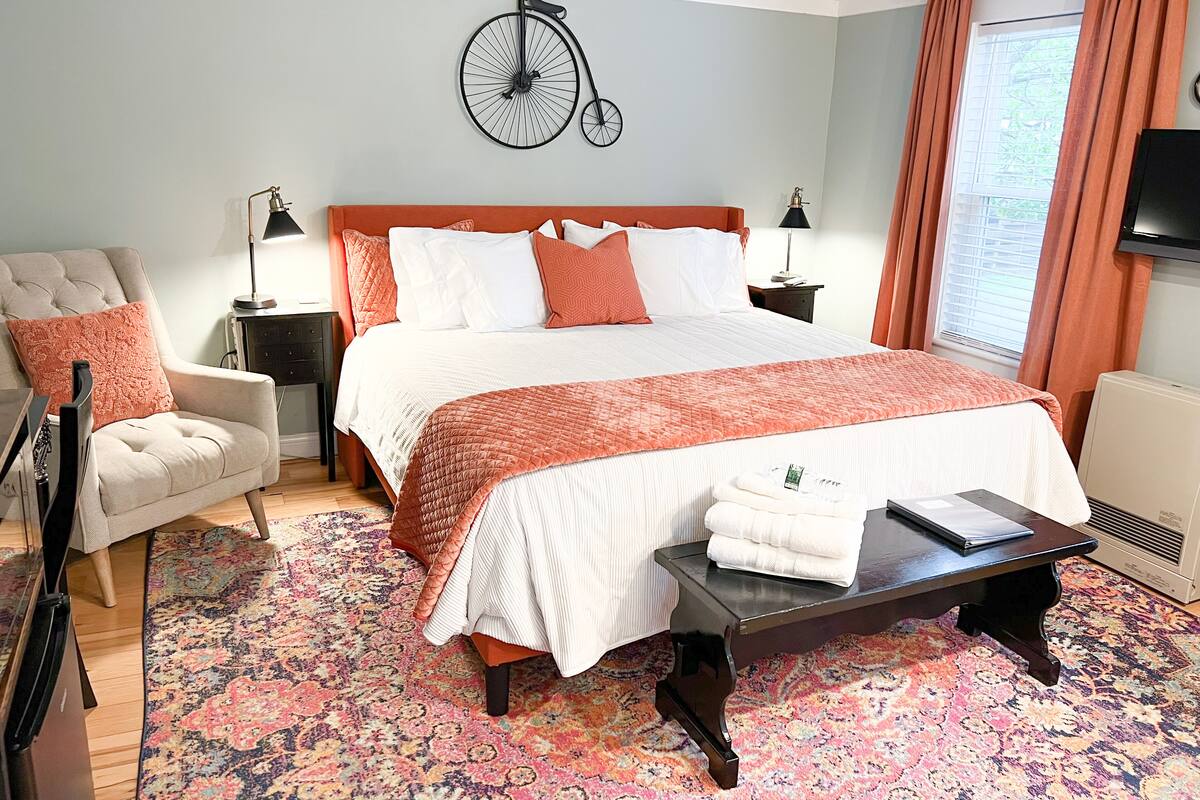 A neatly arranged bedroom with a large bed, a chair, a nightstand, a table, and a wall clock.