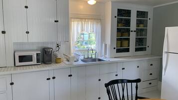 A kitchen with white cabinets, a microwave, a coffee maker, and a sink.