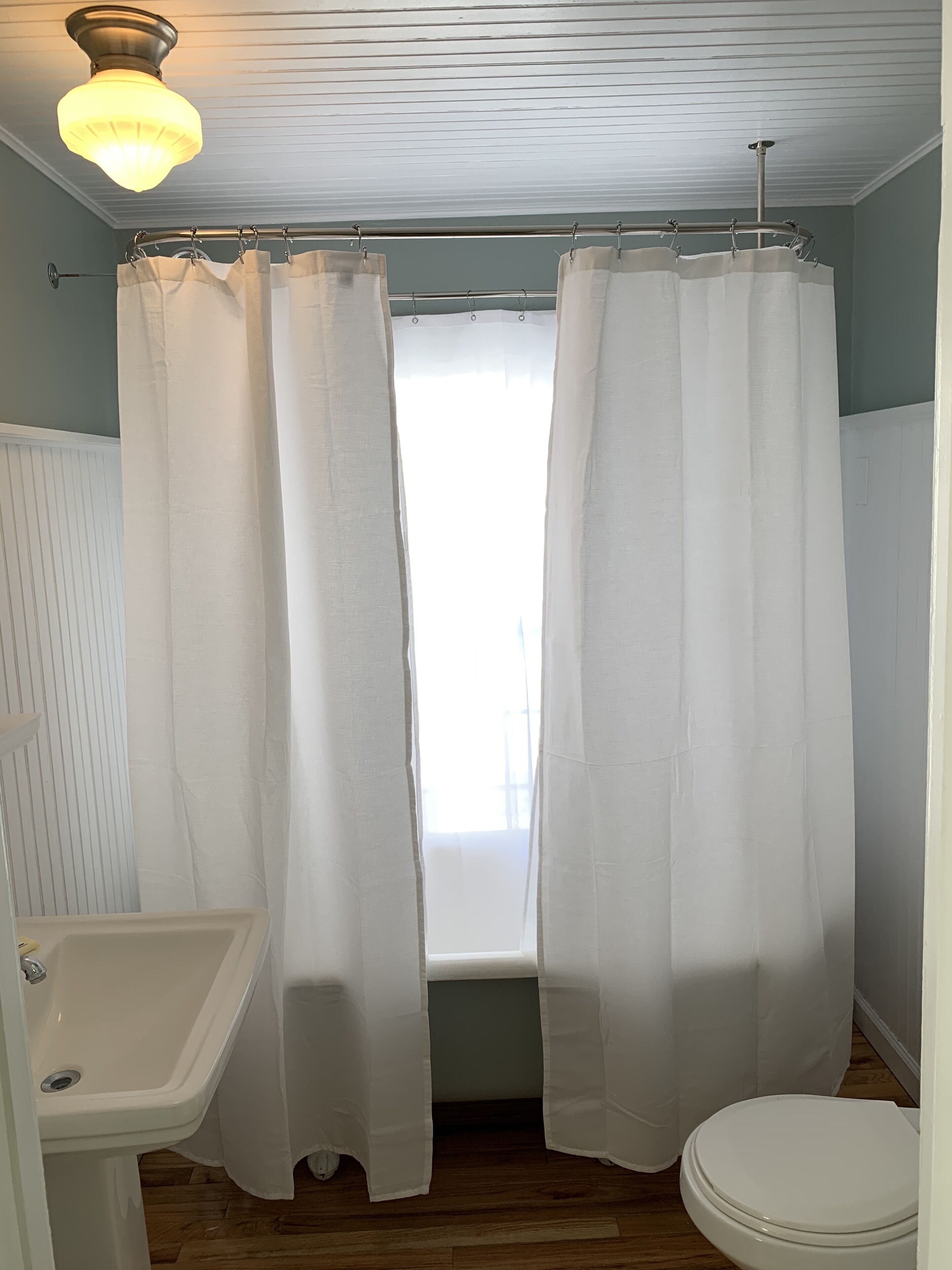 A bathroom with a white sink, toilet, and a window with white curtains.