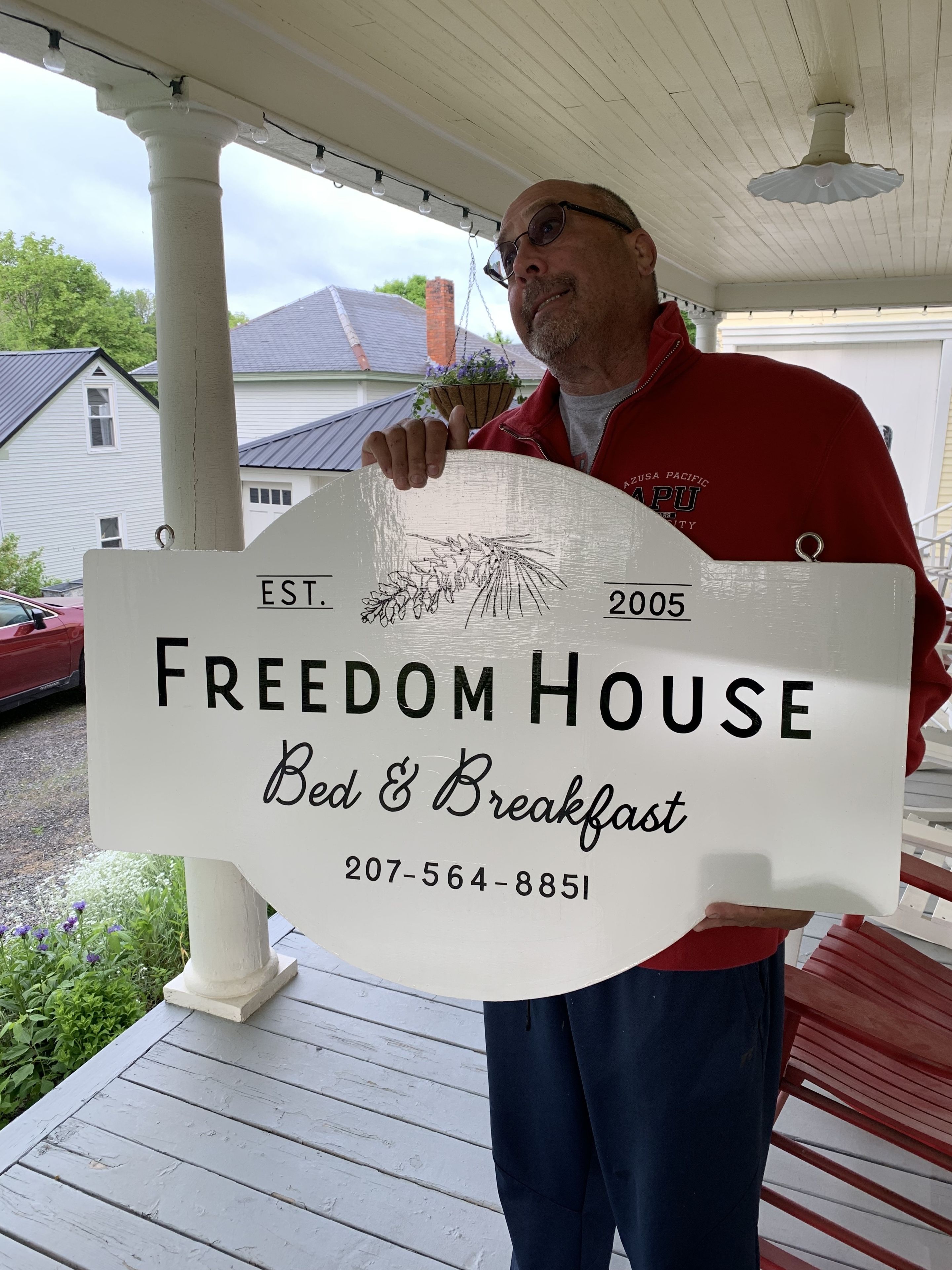 Un uomo che tiene in mano un cartello per Freedom House Bed & Breakfast con un numero di contatto.