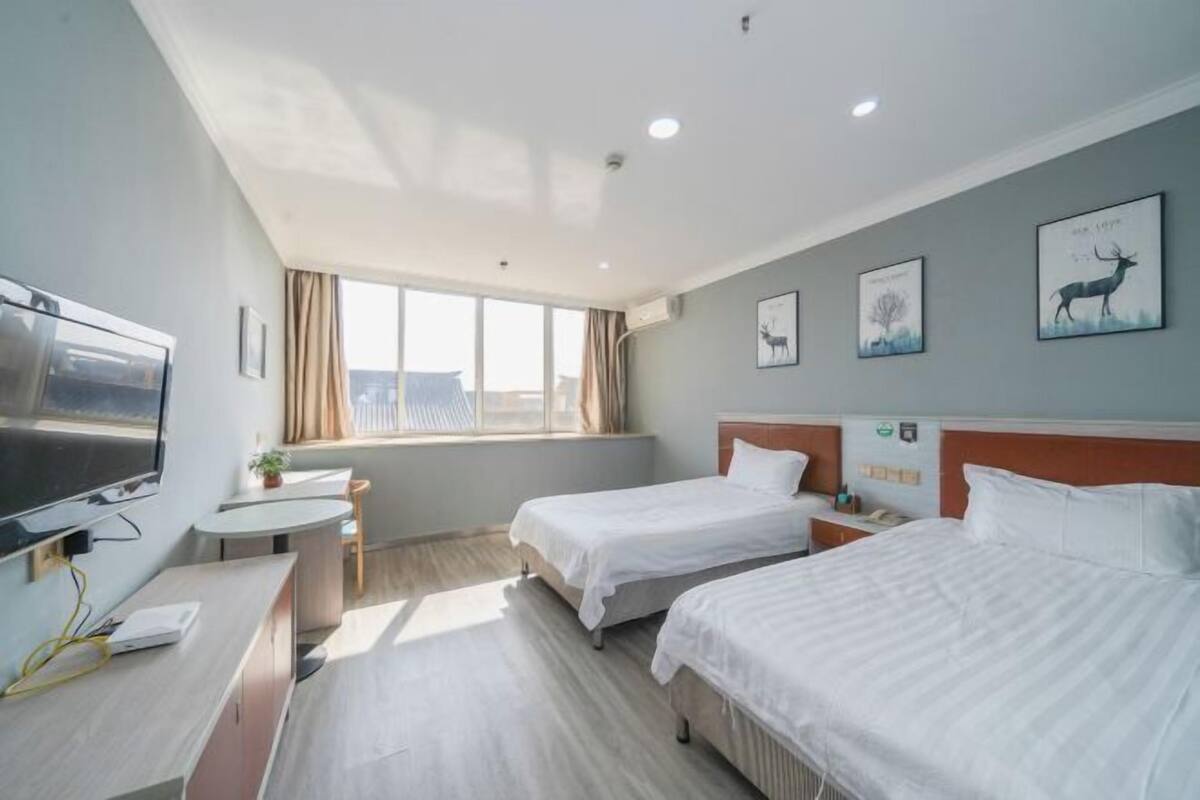 A hotel room with two beds, a desk, a TV, and artwork on the walls.