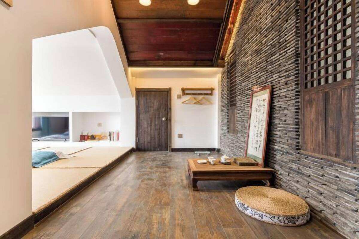 A room with a wooden floor, a bed, a small table, a bench, and a wall with a textured pattern.