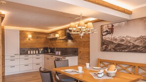 Una cocina moderna con detalles de madera, un comedor con mesa y sillas de madera, y un cuadro de un paisaje montañoso en la pared.