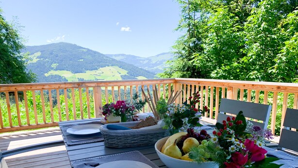 Una mesa de comedor al aire libre con platos, cubiertos, un frutero y arreglos florales.